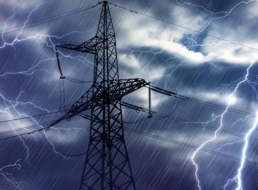 High-voltage power transmission tower during a thunderstorm with lightning bolts and heavy rain.