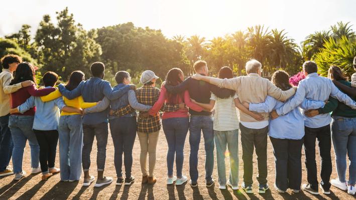 Group of people standing outdoors with arms around each other.