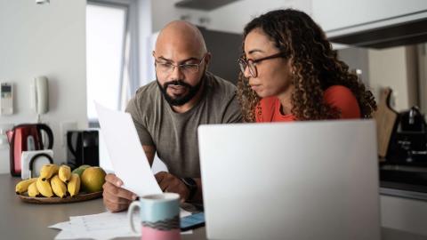 Two people at a kitchen table reviewing papers with a laptop