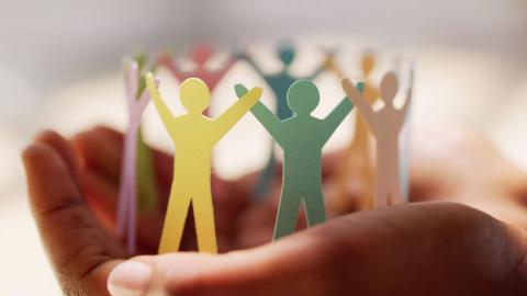 Hands holding a circle of colorful paper cutouts shaped like people.