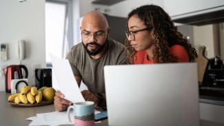 Two people at a kitchen table reviewing papers with a laptop